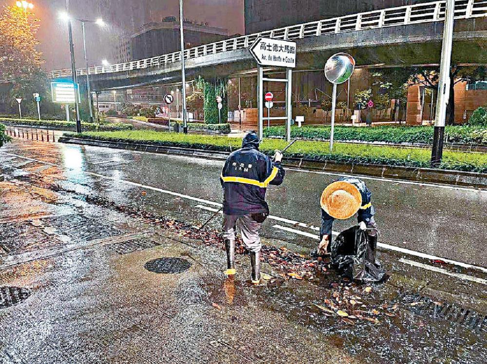 ■在澳門，清潔工掃走在雨水井堆積的垃圾。